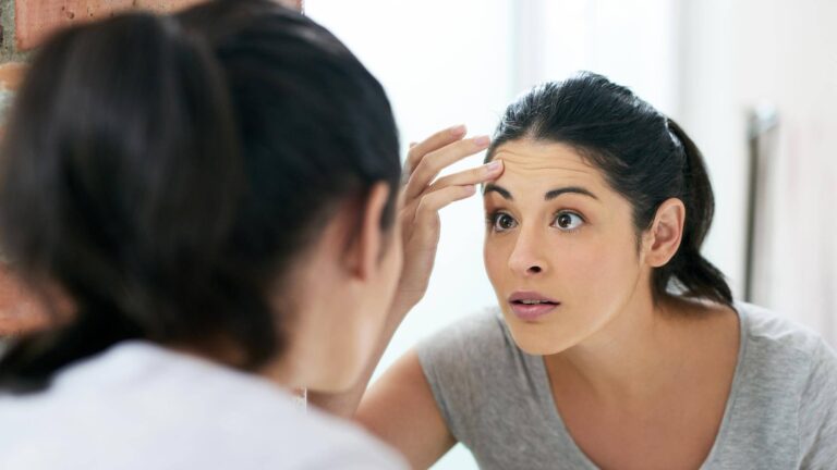 Woman inspecting her skin in the mirror